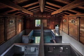 A wooden cabin with two separate bathing areas, each with a small window and a fan.