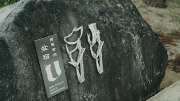 Un grand rocher orné de caractères chinois gravés et une plaque portant des noms.