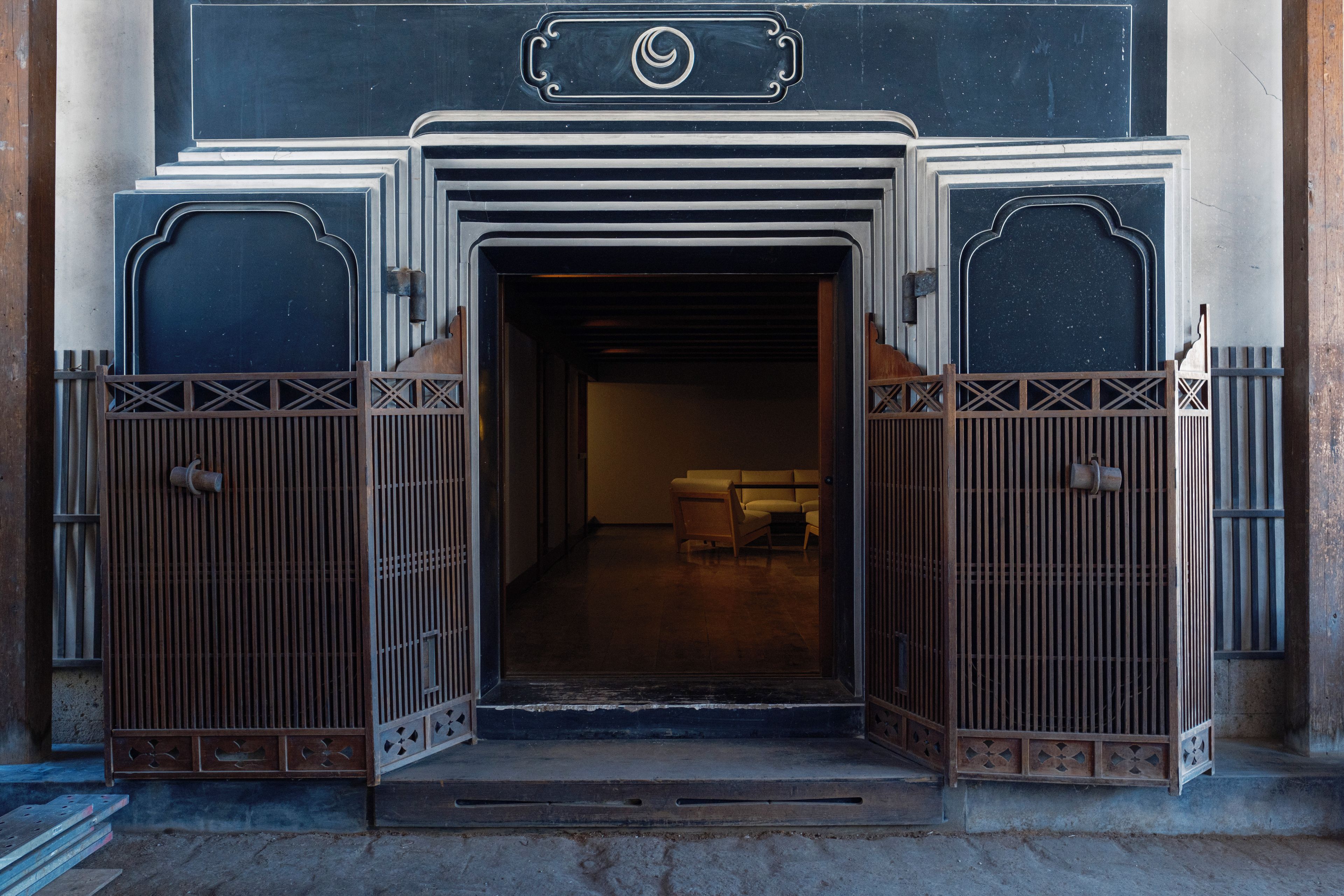 Entrada de un edificio con fachada oscura, un letrero decorativo sobre la puerta y un banco de madera en el interior.