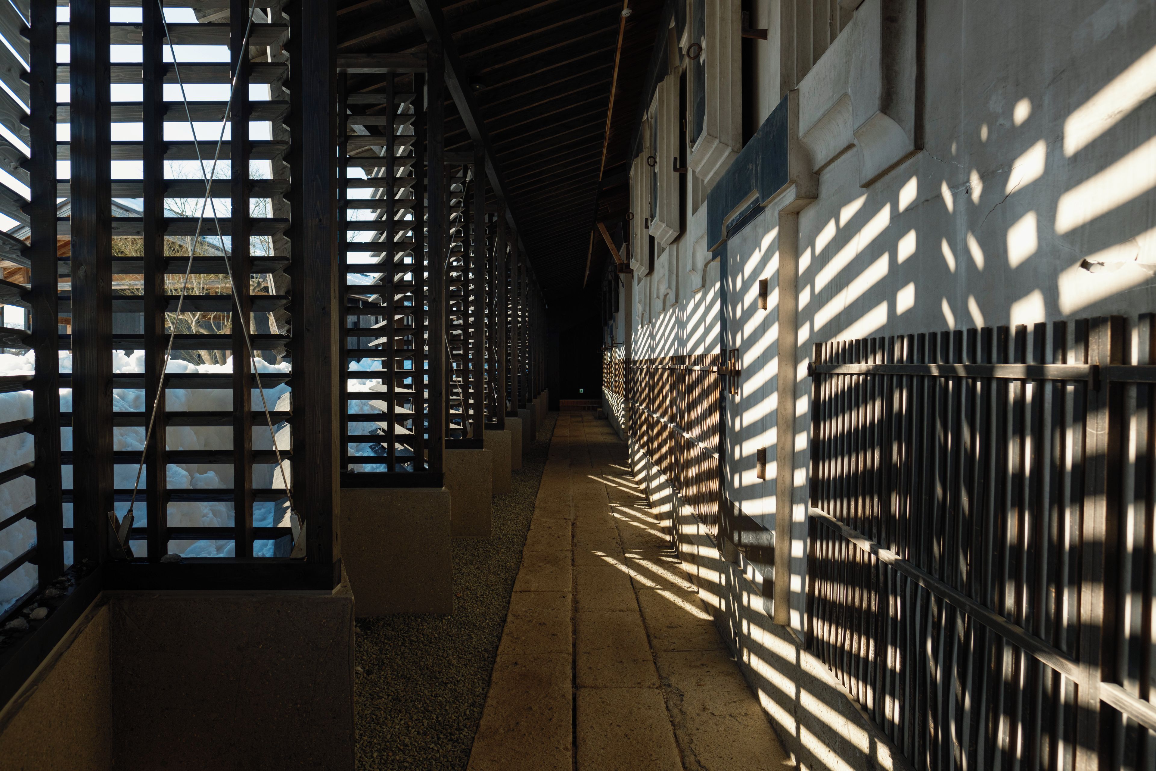 Un corridoio con ringhiere metalliche e pavimento in cemento, che conduce a un edificio con finestre.