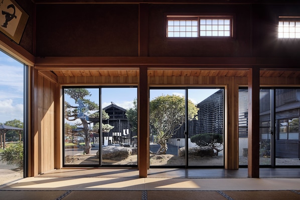A traditional Japanese interior with sliding doors, tatami flooring, and a view of a traditional building.