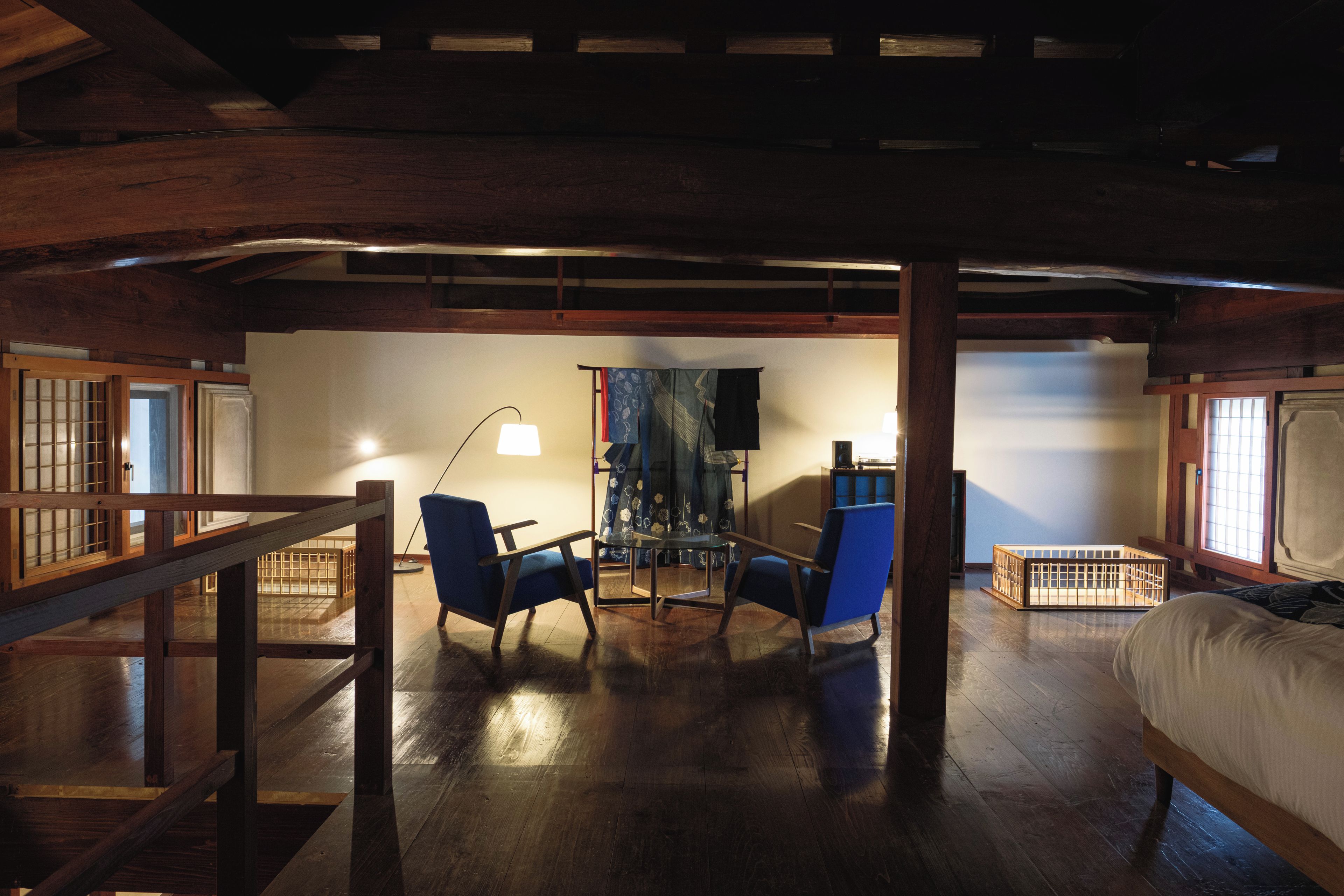 Une pièce avec un plafond en bois, un lit, deux chaises bleues, une petite table et un berceau.