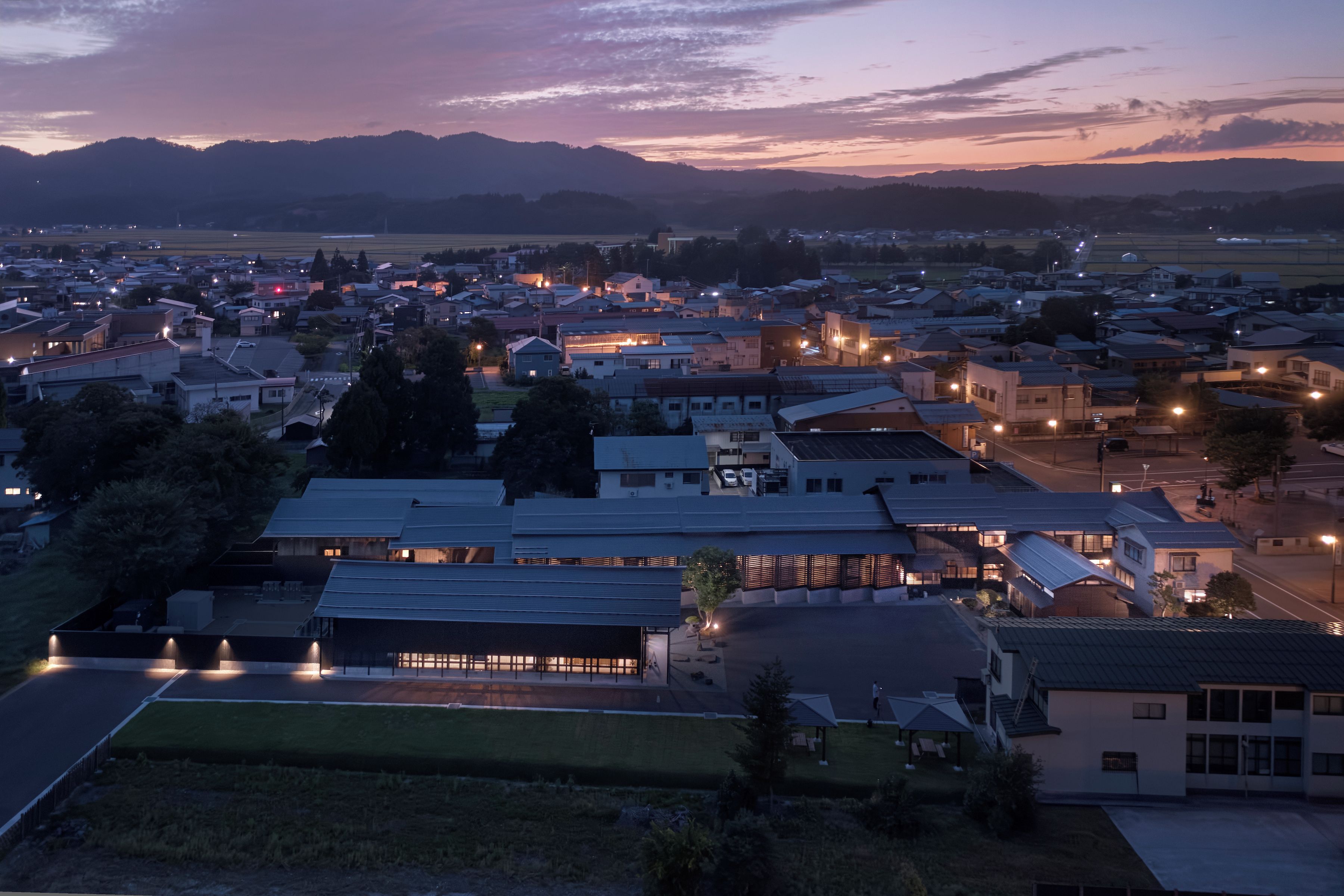A town at dusk with buildings, roads, and distant mountains.
