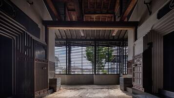 An interior space with a high ceiling, wooden beams, and a large window with metal bars.