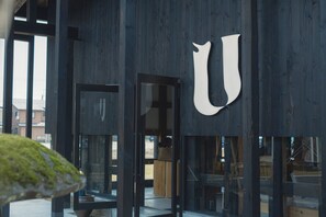 A modern building entrance with a large 'U' sign, glass doors, and a view of the outside.