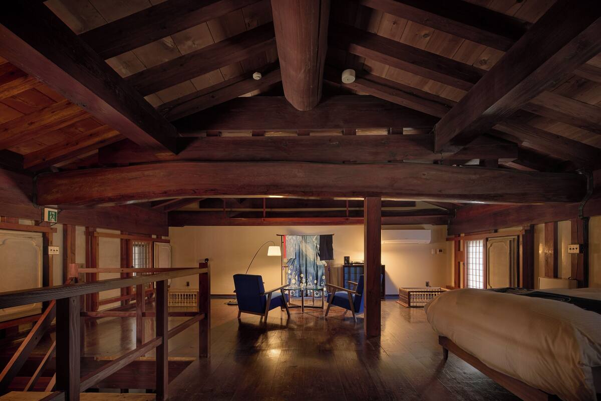 Una habitación amplia con techo alto, vigas de madera, cama, escritorio y silla.