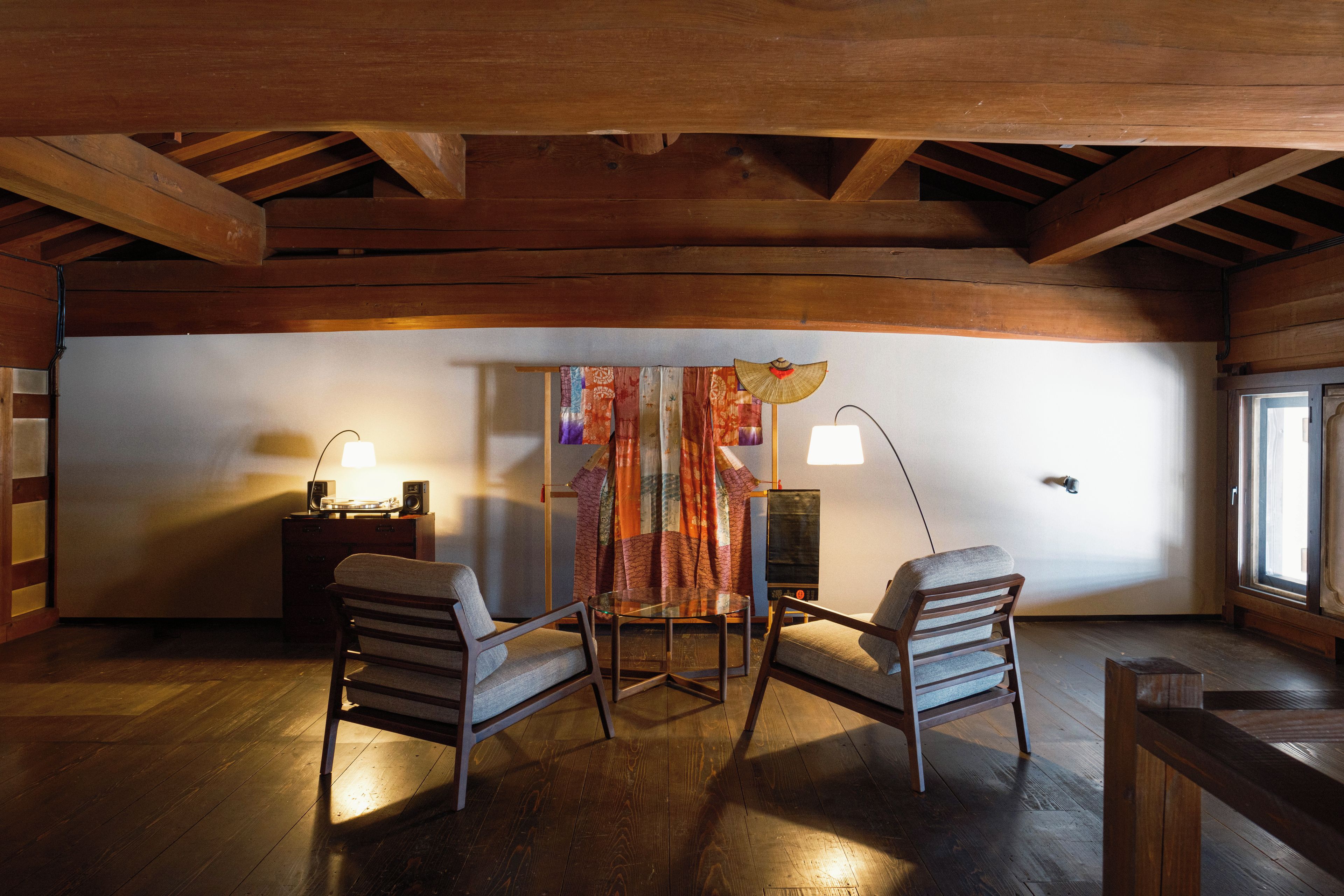 A cozy room with wooden beams, two chairs, a table, and a decorative curtain.