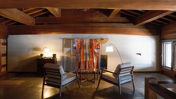 A cozy room with wooden beams, two chairs, a table, and a decorative curtain.