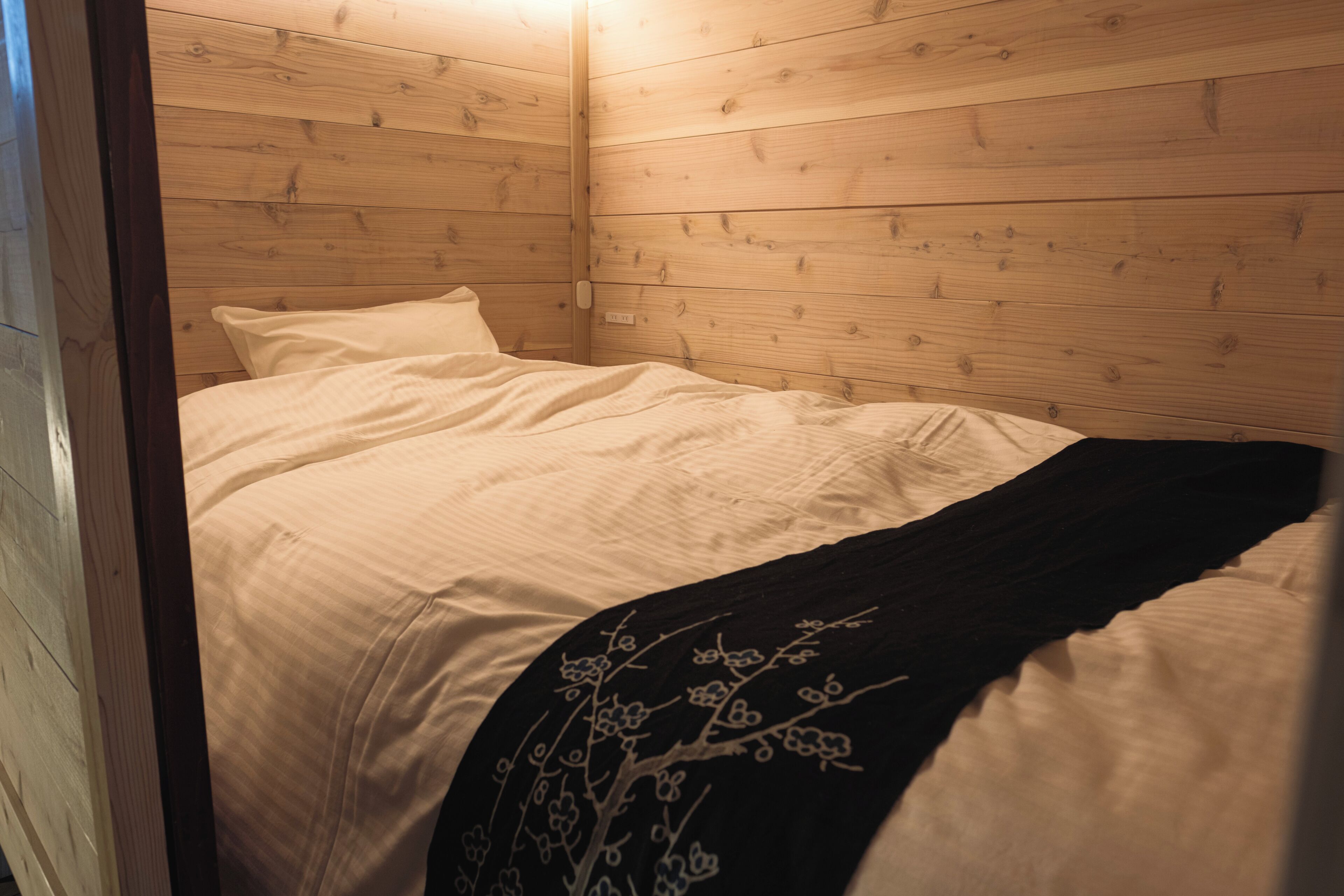 Ein Zimmer mit Holzwänden, einem Bett, weißer Bettwäsche und einer schwarz-blumigen Bordüre.