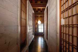 Un estrecho pasillo de madera con una puerta de madera al final, una lámpara colgante y una ventana con luz natural.