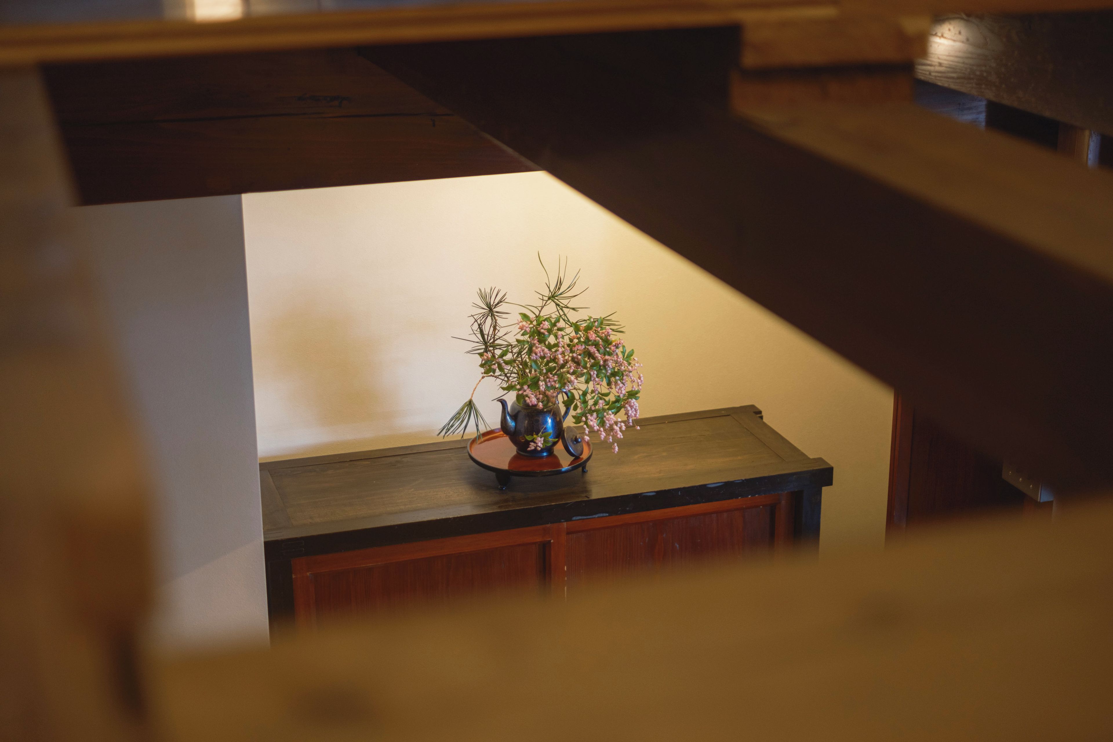 A wooden table with a vase of flowers and a teapot.