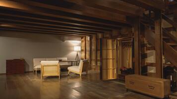 Una habitación con piso de madera, un sofá, una silla, una lámpara, un aparador y una escalera.