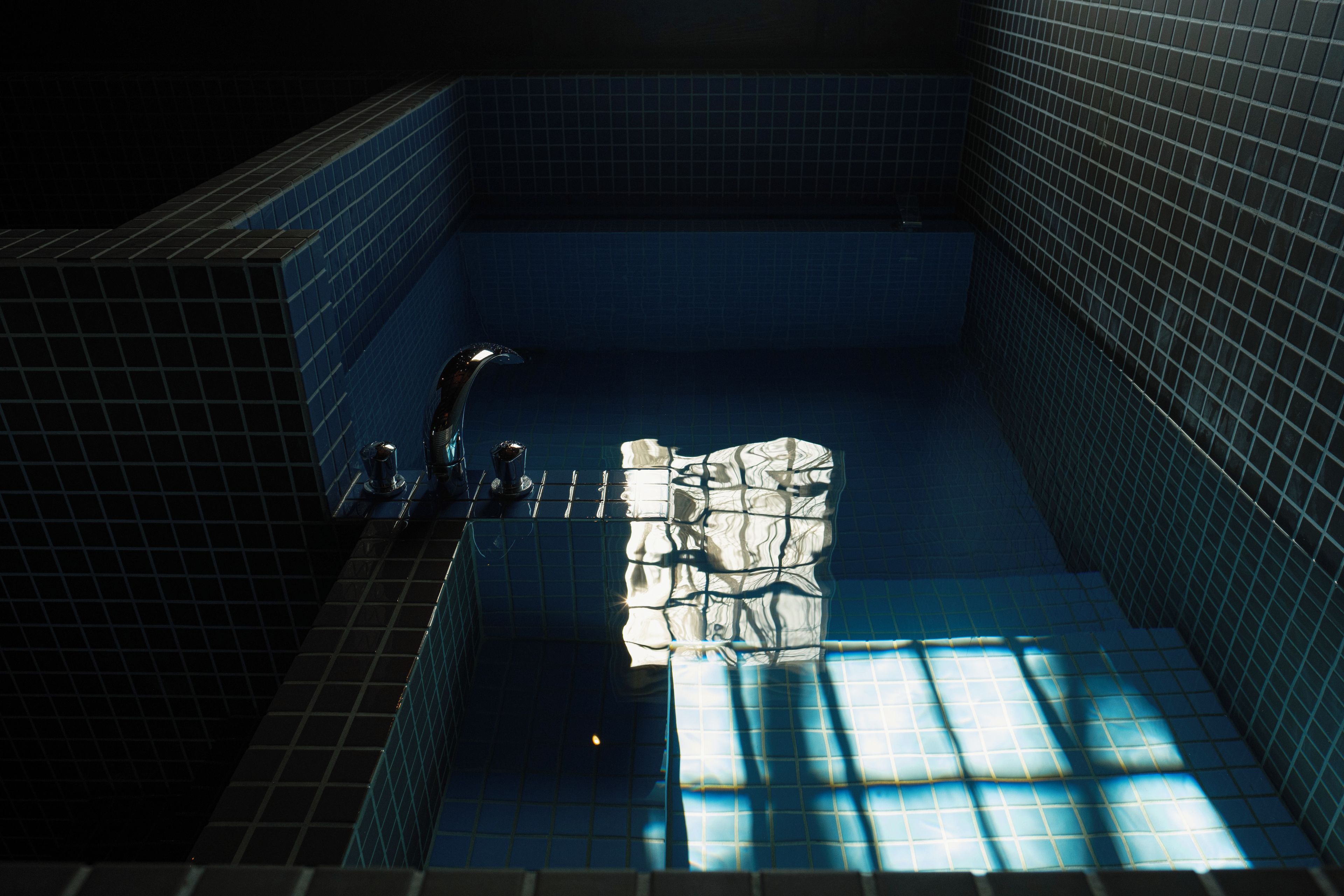 A tiled swimming pool with a faucet and a towel rack.