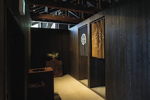 A hallway with wooden walls, a potted plant, and a door with a circular logo. - Bon-yado Uakita Nishimonai (Ugo)