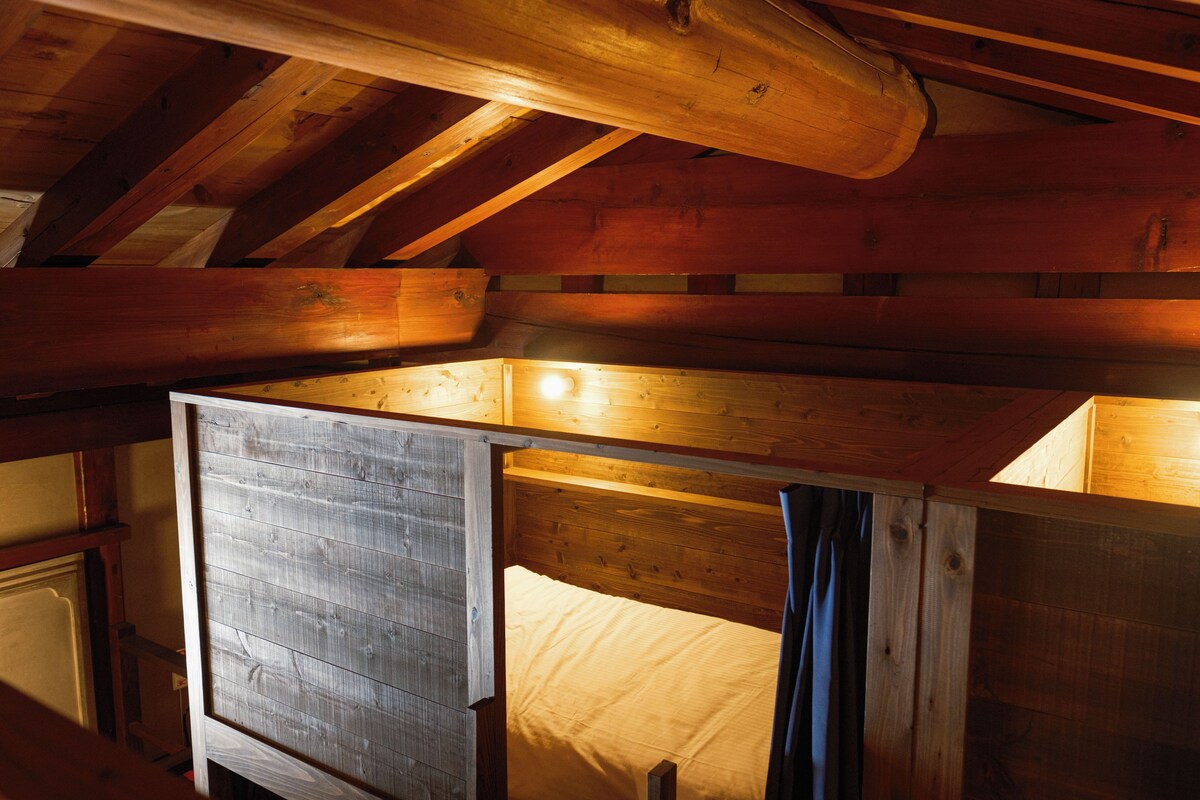 A wooden cabin interior with a loft bed, exposed beams, and a rustic aesthetic.