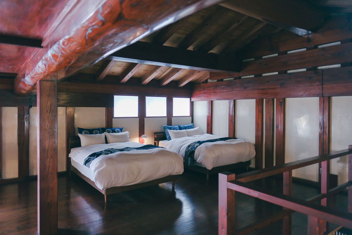 A room with two beds, wooden beams, and large windows.