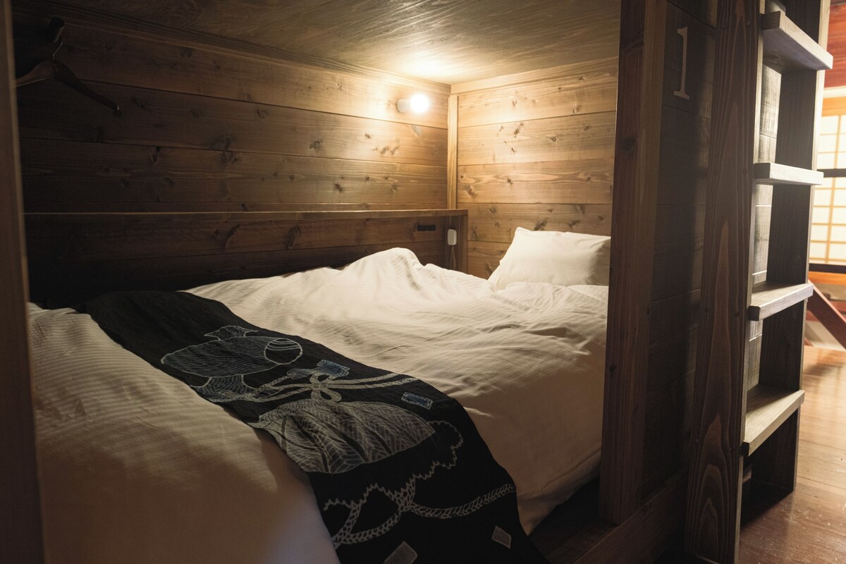 A wooden cabin room with a bed, a hanging light fixture, and a wooden bench.