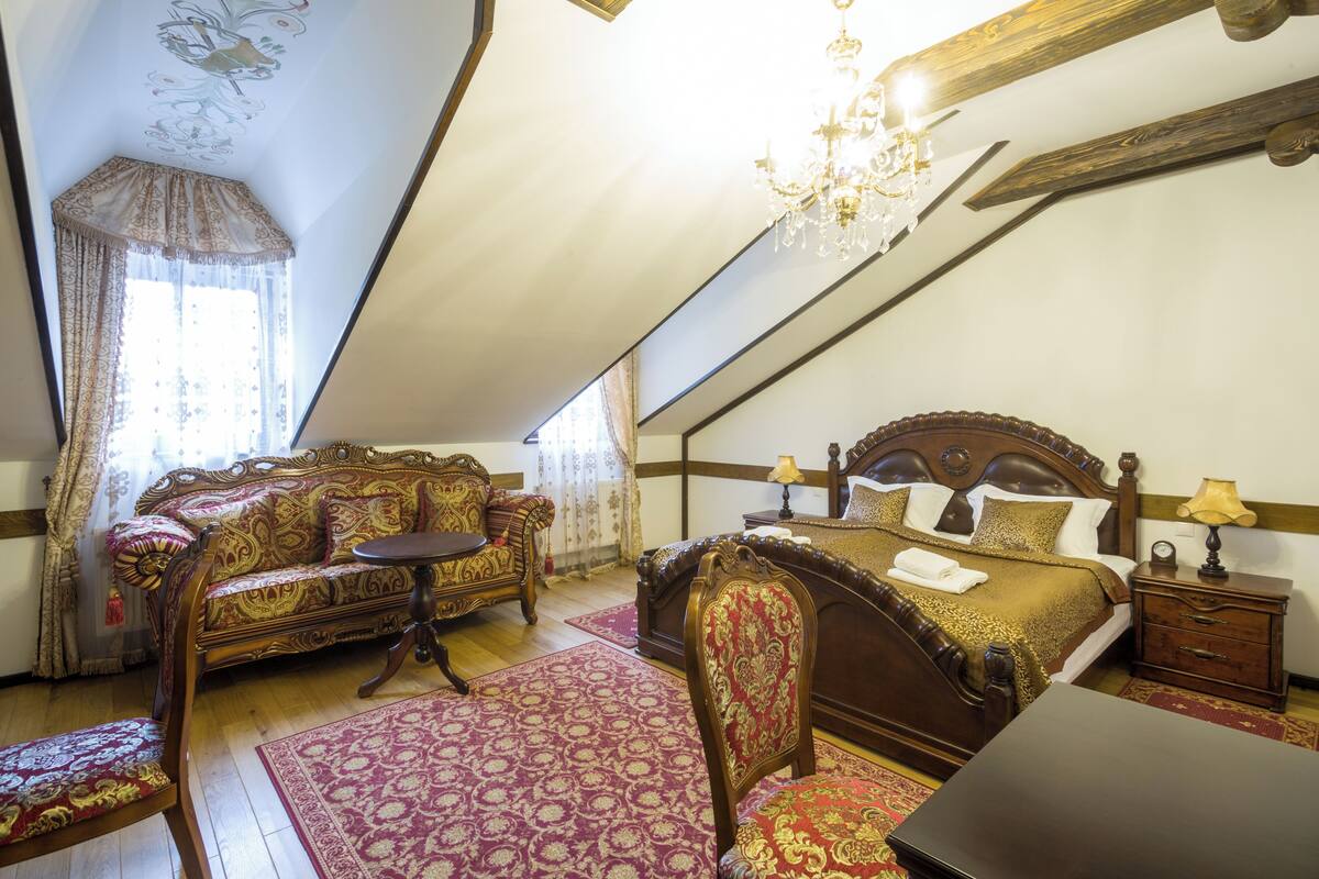 A bedroom with a large bed, a sofa, a chair, a small table, and a nightstand.