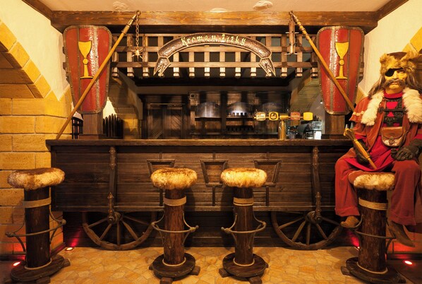 Un espace bar à l’ambiance médiévale, avec des tabourets en bois et un écu décoratif.