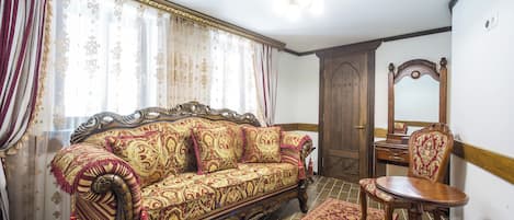 A traditional room with a sofa, a wooden chair, a mirror, and a patterned rug.