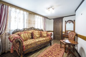 Une pièce au décor traditionnel, avec un canapé, une chaise en bois, un miroir et un tapis à motifs.