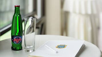 Eine grüne Flasche, ein Glas und ein Heft mit Logo auf einem Tisch.