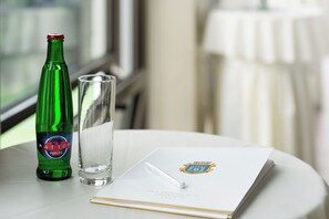 Une bouteille verte, un verre transparent et un livret orné d’un logo, le tout posé sur une table.