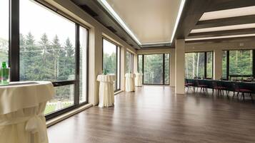 A spacious room with large windows, wooden flooring, and a long table with chairs.