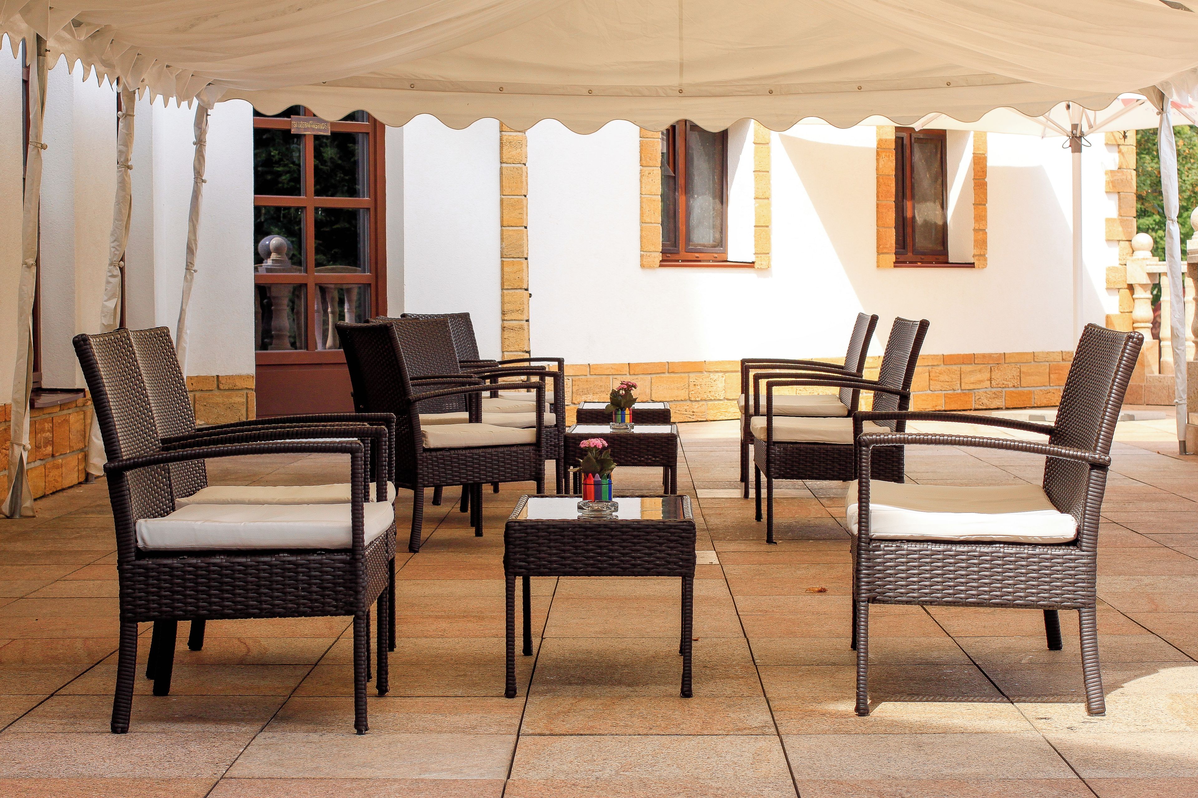 A covered outdoor seating area with wicker furniture and a tiled floor.