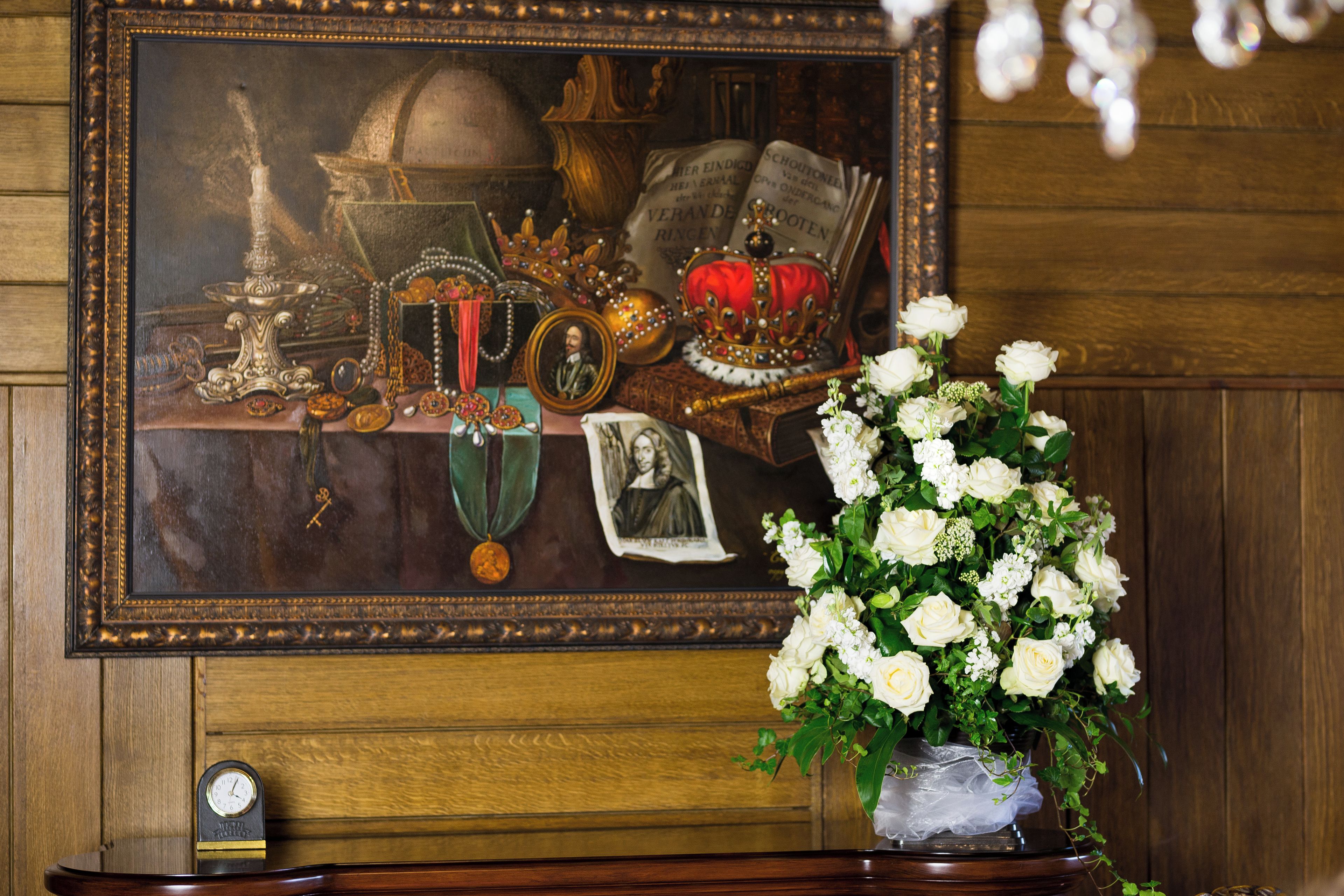 A framed painting with a clock, a vase of white flowers, and a wooden cabinet.