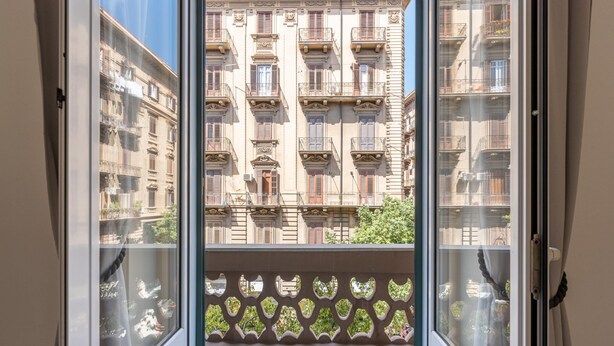 Vista attraverso una porta finestra su un edificio con numerosi balconi e una ringhiera decorata.