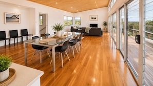 A spacious living area with a glass dining table, black chairs, a sofa, and a TV. - Anchor at Bawley Point (Bawley Point)