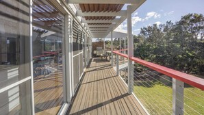 A wooden deck with a glass balustrade, a red railing, and a view of the surrounding greenery. - Anchor at Bawley Point (Bawley Point)