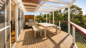 An outdoor deck with a wooden table and bench, a barbecue grill, and a view of greenery. - Anchor at Bawley Point (Bawley Point)