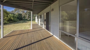 A covered outdoor area with a wooden deck, large sliding glass doors, and a view of a landscaped garden. - Anchor at Bawley Point (Bawley Point)