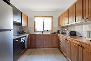 Eine Küche mit Holzschränken, einem Edelstahl-Kühlschrank, einem Herd und einem Fenster mit Vorhängen.
