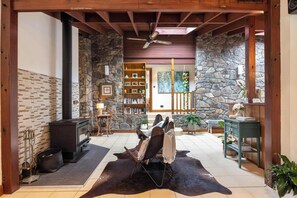 A cozy living room with a stone wall, a fireplace, a bookshelf, and a comfortable seating area. - Banyula in Bawley Point with Pool (Bawley Point)
