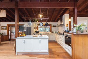 A spacious kitchen with a large island, wooden beams, and a view of the outdoors. - Banyula in Bawley Point with Pool (Bawley Point)