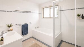 Ein modernes Badezimmer mit einer Badewanne, einem Waschbecken, einer Duschkabine aus Glas und einem Fenster.