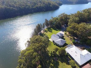 A lakeside property with two large buildings, a grassy area, and dense trees. - Atlantis on Lake Conjola (Conjola Park)