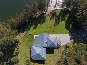 A house with a sloped roof, surrounded by a well-maintained lawn and dense trees. - Atlantis on Lake Conjola (Conjola Park)