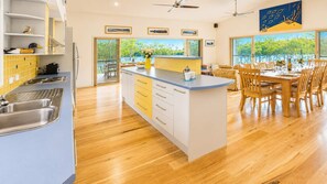 A modern kitchen with a central island, wooden flooring, and a dining area with a view of the outdoors. - Atlantis on Lake Conjola (Conjola Park)