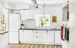 A kitchen with white cabinets, a refrigerator, a coffee maker, a sink, and a window with a plant. - 5 bedroom pet friendly home in Sjöbo (Sjöbo)
