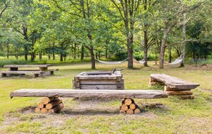 Een rustieke omgeving buiten met een houten bank, een hangmat en picknicktafels.