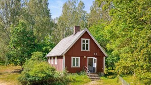 A small, single-story cabin with a red exterior, white trim, and a chimney, surrounded by dense greenery. - 5 bedroom pet friendly home in Sjöbo (Sjöbo)