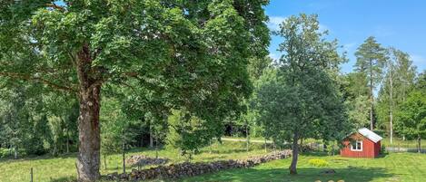 Un paysage rural avec un grand arbre, un mur de pierre et un bâtiment rouge.