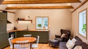 Una cocina con vigas de madera, una mesa de comedor con sillas, un sofá y una ventana con vistas a árboles.
