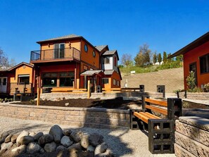 A multi-story building with a balcony, a stone retaining wall, and a gravel area with rocks. - .50 Acre Property - Spacious Living with Wood Accents - Sleeps up to 20 (Vernon)