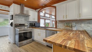 A kitchen with white cabinets, stainless steel appliances, a wooden countertop, and a stone backsplash. - .50 Acre Property - Spacious Living with Wood Accents - Sleeps up to 20 (Vernon)
