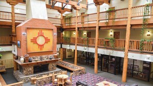 Un'ampia hall con un camino centrale, diverse zone relax e un balcone con ringhiere in legno.